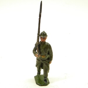 May include: A green painted toy soldier figurine holding a rifle, wearing a helmet and standing on a green base.