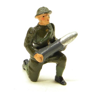 May include: A green painted toy soldier figurine kneeling and holding a grey and silver rocket launcher.