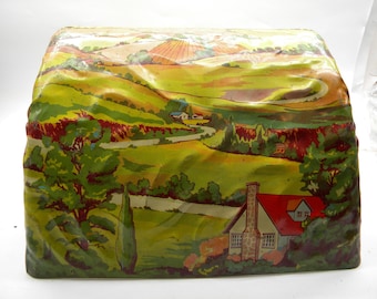 May include: A vintage tin toy train tunnel with a colorful countryside scene painted on the exterior. The scene includes rolling hills, a winding road, trees, and a small house with a red roof.