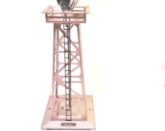 Puede incluir: Una torre de baliza de metal plateado con una escalera y una lámpara. La torre tiene una base cuadrada y una plataforma en la parte superior. La lámpara tiene lentes rojas y verdes.