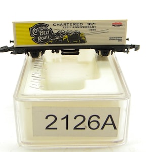 May include: A model train car with the text "Cotton Belt Route" and "Chartered 1871 125th Anniversary 1996". The car is cream and yellow with black wheels and is in a clear plastic case with the number "2126A".