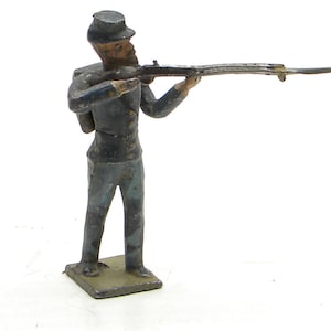 May include: A blue and gray painted lead toy soldier figurine holding a rifle. The soldier is wearing a blue uniform and a black hat. The soldier is standing on a gray base.