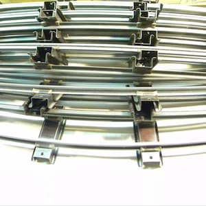Könnte beinhalten: Ein Stapel gebogener Modellbahngleise in Silber. Jedes Gleisstück hat ein gebogenes Schienenprofil mit Metallverbindern. Die Gleise sind so konzipiert, dass sie miteinander verbunden werden können, um einen kreisförmigen oder ovalen Gleisverlauf zu bilden.