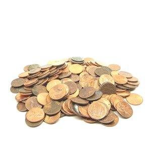 May include: A pile of copper-colored pennies, some with visible details of Abraham Lincoln's profile and the Lincoln Memorial. The coins are scattered on a white background, creating a contrast of textures and colors.