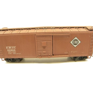 May include: A brown boxcar model train car with the words "ERIE 60596" and a diamond-shaped logo with the word "ERIE" printed on it.