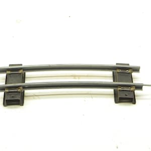Könnte beinhalten: Zwei gebogene, parallele Metall-Zugschienen mit schwarzen Stützen. Die Schienen sind grau und leicht gebogen. Die Stützen sind rechteckig und haben kleine Metallclips. Das Bild befindet sich auf weißem Hintergrund.
