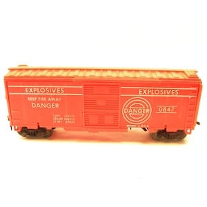 May include: A red toy train car with "EXPLOSIVES" printed on the side. The car has a black "DANGER" sign with a circle around it. The car also has the number "0847" printed on the side.