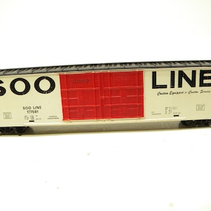 May include: A white model train carriage with black lettering that reads "SOO LINE" and "Custom Equipped & Custom Service". The carriage has red doors with a grid pattern and the number "177581" printed on the side.