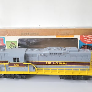 May include: A grey and yellow Erie Lackawanna model train engine, with the number 8760. The engine has a brown stripe and is in front of a cardboard box with the words "ENGINE" and "Pullmor Motor".