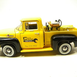 May include: Yellow 1956 Ford F-100 pickup truck model with a black bed and a black fender. The truck has a black and red "Al's Custom Repair" logo on the side and the phone number "CC4-7255".
