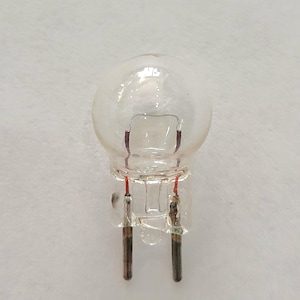 May include: A clear glass light bulb with two metal prongs. The bulb is small and round, with a clear glass base.