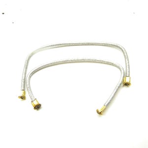 May include: Two silver-coloured elastic cords with gold-coloured metal tips. The cords are looped together.