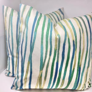 May include: Two decorative throw pillows with a white background and a vertical watercolor stripe pattern in shades of blue, green, and yellow. The pillows are square and appear to be made of fabric.