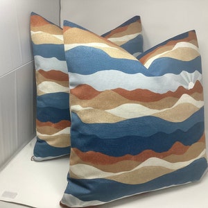 May include: Two decorative throw pillows with a blue, white, and brown abstract mountain range pattern. The pillows have a subtle shimmer.