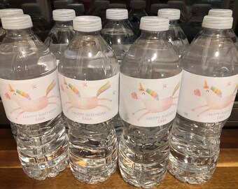 Könnte beinhalten: Ein Set aus durchsichtigen Plastikwasserflaschen mit personalisierten Etiketten, die ein pinkfarbenes Einhorn mit einer Regenbogenmähne und dem Text "Happy Birthday Ema" zeigen.