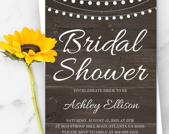 May include: A rustic woodgrain background with white string lights and the text "Bridal Shower" in white cursive font. The text "To Celebrate Bride to Be" is in white font. The bride's name, "Ashley Ellison", is in white cursive font. The date and time of the bridal shower are listed below, along with the address and RSVP information. The text "Ashley is registered at Target" is in white font.