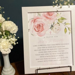 Puede incluir: Una impresi&oacute;n enmarcada blanca con un dise&ntilde;o floral rosa y una oraci&oacute;n para Hayley & Carrill. La oraci&oacute;n dice: "Se&ntilde;or, rodea a esta ni&ntilde;a con bondad. Gu&iacute;ala en tu luz cada d&iacute;a. Ay&uacute;dala a caminar por el camino que has elegido. Gu&iacute;a sus pasos a lo largo del camino. Ens&eacute;&ntilde;ale, Se&ntilde;or, a confiar en tu sabidur&iacute;a con una fe de arriba. Mantenla a salvo de todo da&ntilde;o, y bend&iacute;cela siempre con tu gracia y amor."
