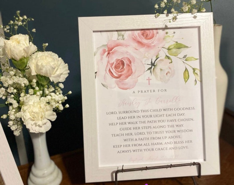 Puede incluir: Una impresi&oacute;n enmarcada blanca con un dise&ntilde;o floral rosa y una oraci&oacute;n para Hayley & Carrill. La oraci&oacute;n dice: "Se&ntilde;or, rodea a esta ni&ntilde;a con bondad. Gu&iacute;ala en tu luz cada d&iacute;a. Ay&uacute;dala a caminar por el camino que has elegido. Gu&iacute;a sus pasos a lo largo del camino. Ens&eacute;&ntilde;ale, Se&ntilde;or, a confiar en tu sabidur&iacute;a con una fe de arriba. Mantenla a salvo de todo da&ntilde;o, y bend&iacute;cela siempre con tu gracia y amor."