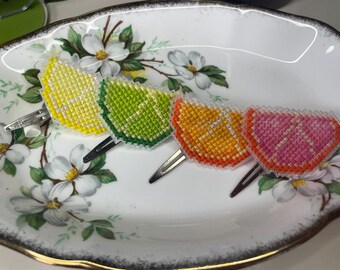 May include: Four embroidered citrus fruit hair clips on a white plate with a floral pattern. The clips are yellow, green, orange, and pink.