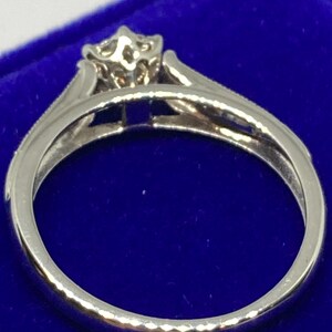 May include: A silver ring with a floral-inspired design at the center. The ring features a delicate band and a raised setting for the central stone. The ring is set against a blue background.