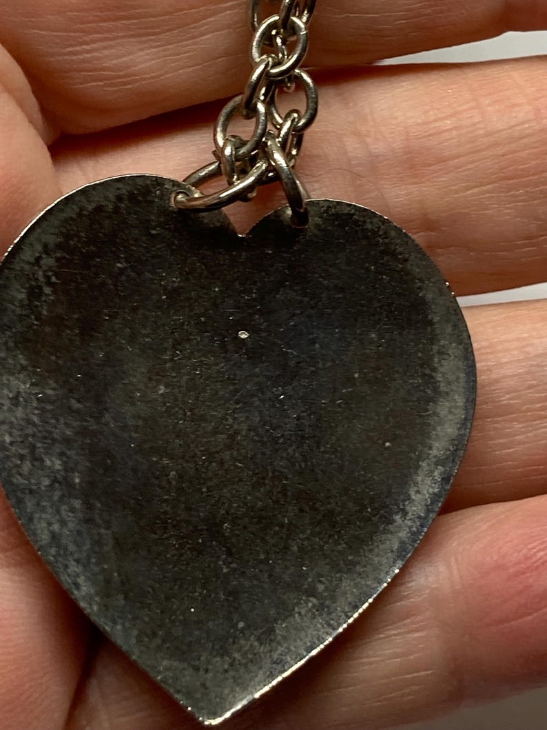 May include: A silver heart-shaped keychain pendant with a chain. The pendant has a worn, textured surface. The keychain is a simple, classic design.