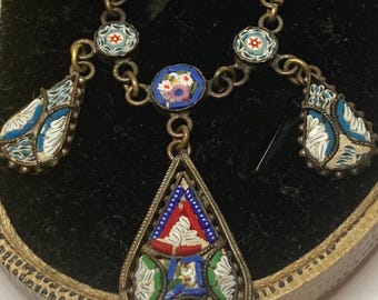 May include: Vintage mosaic necklace with a silver chain. The necklace features a central teardrop pendant and smaller floral and geometric mosaic designs in shades of blue, red, white, and green. The necklace is displayed on a black surface.