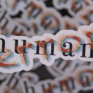 May include: A sticker with the word "human" written in black text on a white background. The word is surrounded by a colorful, abstract design in shades of blue, green, orange, and red.