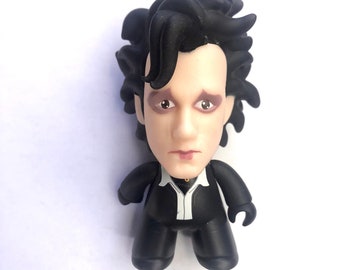 May include: Black and white vinyl figure of a man with black hair and a black suit. The figure has a serious expression on its face.