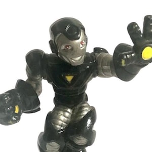 May include: Black and silver action figure of a superhero with a yellow glowing hand. The figure is standing on a gray base.