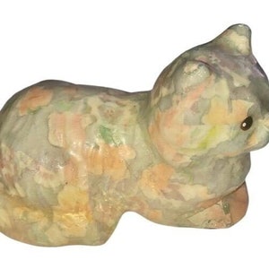 May include: A ceramic cat figurine with a light green, pink, and yellow floral pattern. The cat is lying down with its head turned to the side.