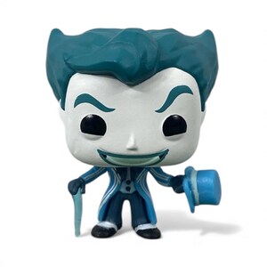 May include: A Funko Pop vinyl figure of a character with teal hair, eyebrows, and a matching suit. The figure has a white face with black eyes and a green smile. It holds a blue cane and a blue top hat.