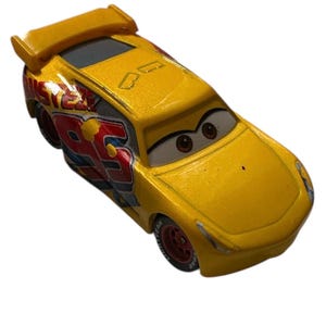 May include: A yellow toy race car with the number 95 in red and blue on the side. The car has a spoiler and cartoon eyes. The car is a die-cast model.