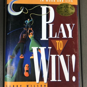 May include: A book cover with a colorful illustration of people reaching up to a crescent moon. The title of the book is "Play to Win!" and the subtitle is "Choosing Growth Over Fear in Work and Life". The book cover also features a gold sticker that says "Book of the Year Award Winner".