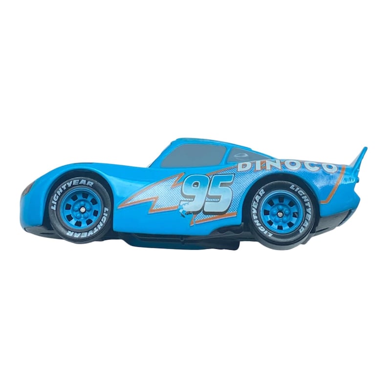 May include: A light blue toy race car with the number 95 on the side. The car has black tires with the word "LIGHTYEAR" on the sidewalls. The car has a lightning bolt design and the word "DINOCO" on the back.