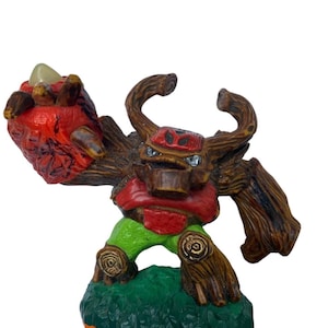 May include: A detailed figurine of a tree-like creature with a brown wooden body, red chest, and green legs. The figure has a large, textured fist and stands on a green base. The figure has a menacing expression.