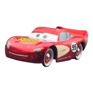 Peut inclure: Une voiture jouet rouge avec le num&eacute;ro 95 sur le c&ocirc;t&eacute; et le nom "Rust-eze" sur le capot. La voiture a des pneus blancs et des yeux bleus. La voiture est un personnage de Flash McQueen du film Cars.