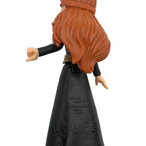 May include: A plastic figurine of a character with long, flowing auburn hair and a braided crown. The figure wears a black dress with a flared skirt and black boots. The back of the figure is visible, with the arms extended.