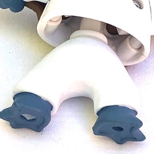 May include: A white plastic toy robot with black feet and a brown arm. The robot has a round head with a hole in the top.