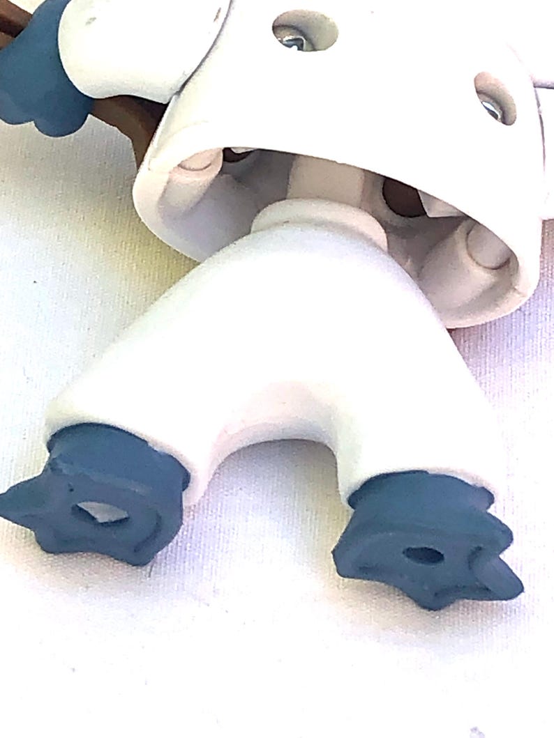 May include: A white plastic toy robot with black feet and a brown arm. The robot has a round head with a hole in the top.