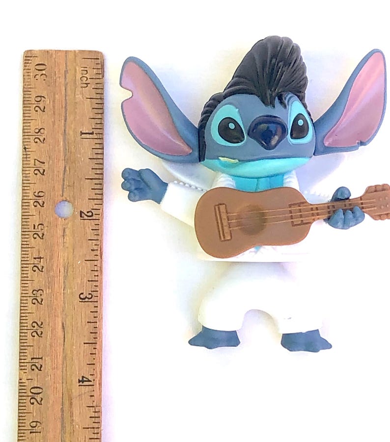 May include: Blue Stitch character figurine playing a brown guitar. Stitch is wearing a white jumpsuit with a black pompadour hairstyle. The figurine is approximately 4 inches tall.
