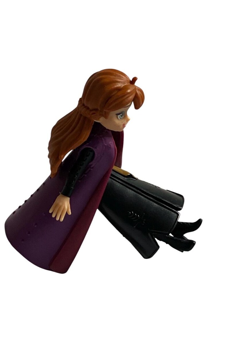 May include: A purple and burgundy dress with a black bodice and long brown hair. The doll is sitting with its legs crossed and is wearing black shoes.