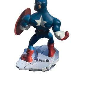 May include: A Captain America figurine in a dynamic pose, featuring a blue and white costume with a star emblem, red boots, and a shield. The figure stands on a rocky base, showcasing a classic superhero design.