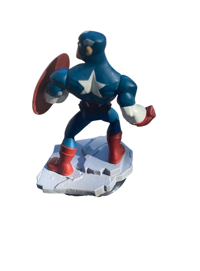 May include: A Captain America figurine in a dynamic pose, featuring a blue and white costume with a star emblem, red boots, and a shield. The figure stands on a rocky base, showcasing a classic superhero design.