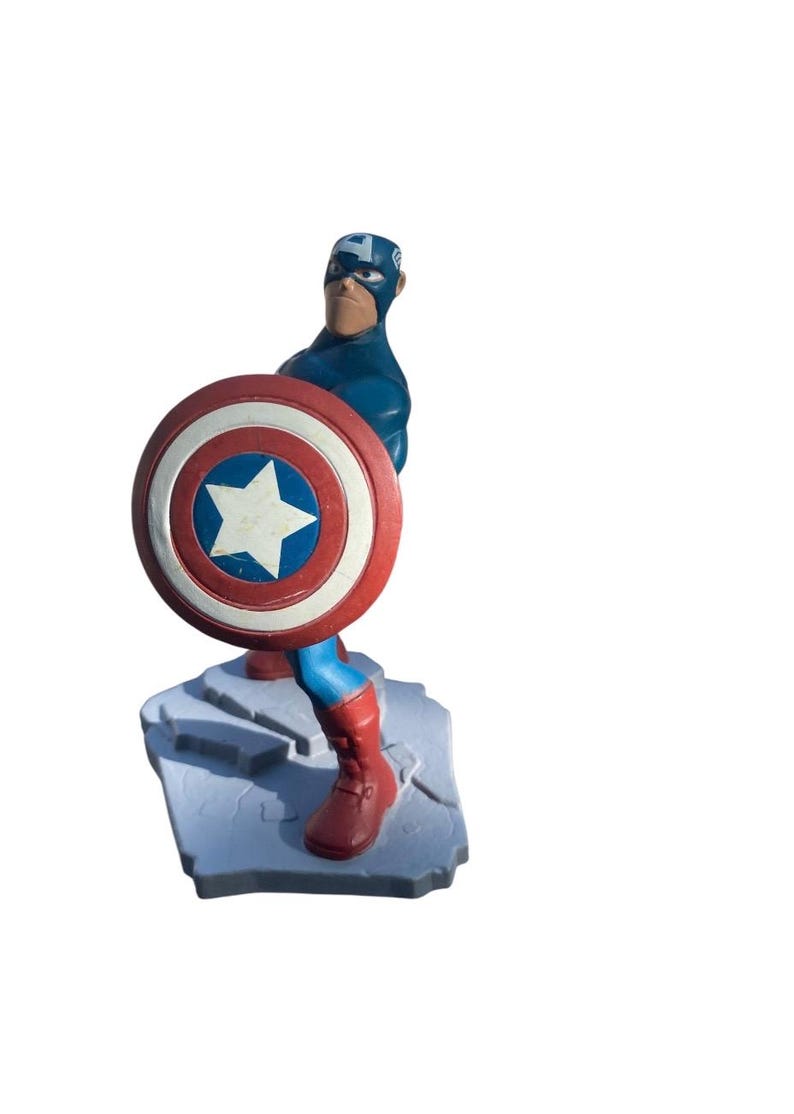 May include: A Captain America figurine in a dynamic pose, holding his iconic shield. The figure is predominantly blue, red, and white, standing on a gray base. The shield features a white star in a blue circle.