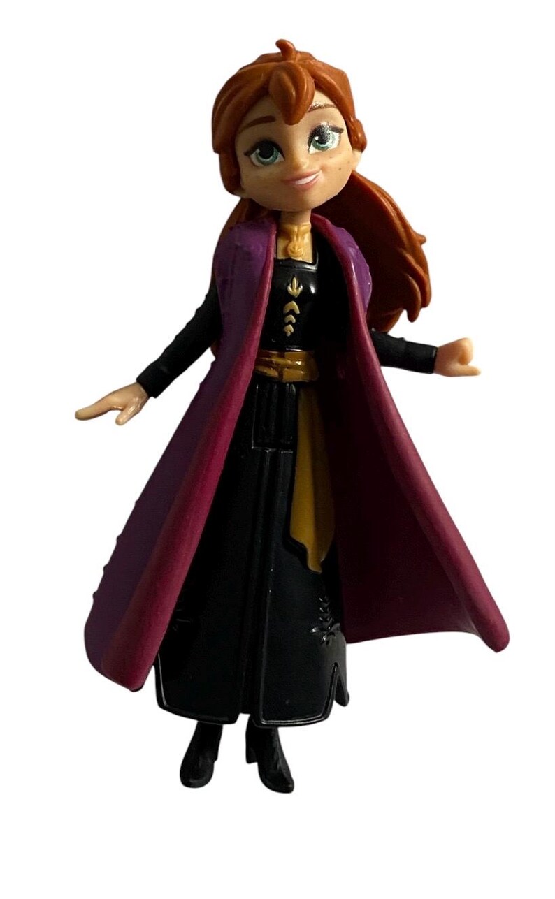 May include: A small plastic figurine of Anna from the Disney film Frozen. She is wearing a black dress with a purple cape, a gold belt, and a gold necklace. Her hair is red and pulled back in a ponytail.