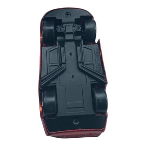 Peut inclure: Vue du dessous d'une voiture jouet rouge avec des roues noires et un ch&acirc;ssis noir. La voiture a un design a&eacute;rodynamique et est en plastique. Le logo Disney/Pixar est visible sur le c&ocirc;t&eacute;.