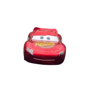 Peut inclure: Une voiture jouet rouge avec le nom "Rust-eze" et le num&eacute;ro "95" imprim&eacute;s. La voiture a un pare-brise blanc et des yeux bleus. C'est un jouet.