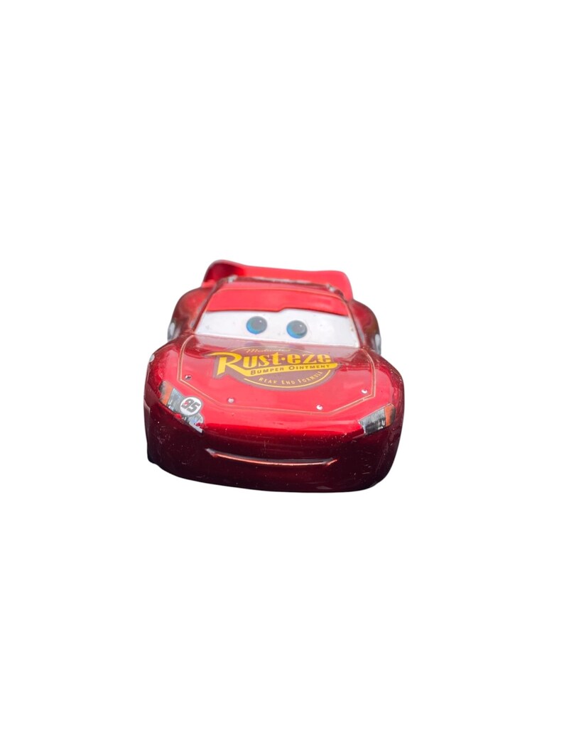 Peut inclure: Une voiture jouet rouge avec le nom "Rust-eze" et le num&eacute;ro "95" imprim&eacute;s. La voiture a un pare-brise blanc et des yeux bleus. C'est un jouet.