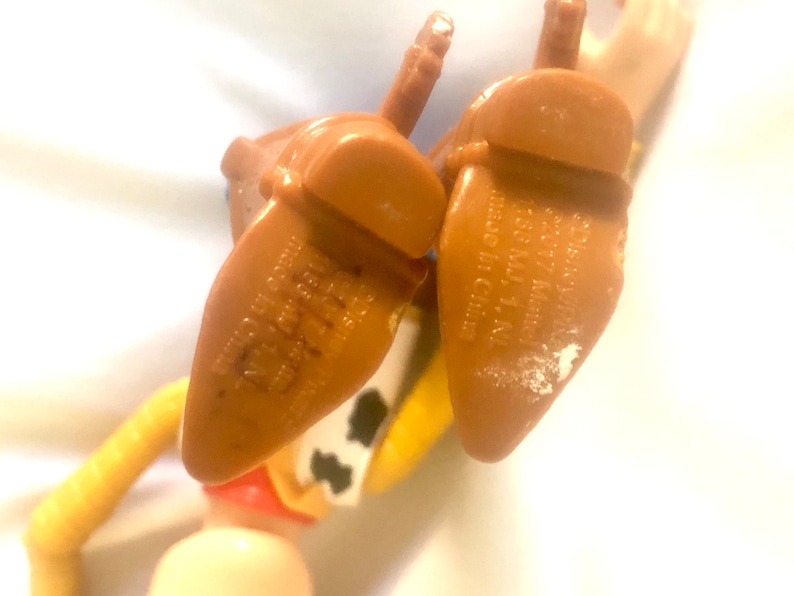 May include: Close-up of the bottom of a brown plastic toy cowboy boot with the text "Disney 22017 Mate 1158 MJ, 1, NI made in China" printed on the bottom.