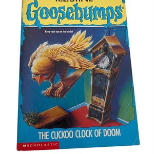 May include: A paperback book titled "Goosebumps: The Cuckoo Clock of Doom" by R.L. Stine. The cover features a menacing bird perched on a wooden beam, a grandfather clock, and the text "Keep your eye on the birdie!" in a blue and yellow design.